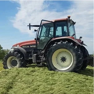 Tracteur New Holland marron sur un grand tas d'herbe coupée sous un ciel bleu nuageux à Ambillou près de Tours en Indre-et-Loire 37
